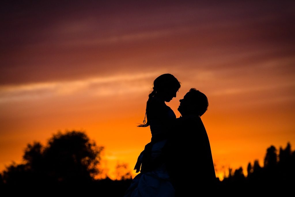 A couple in the sunset. The husband lifts his wife up in the air.