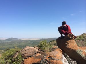 Maasai man sitting on a stone high above the Mara. He is enjoying the view.