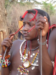 A young Maasai warrior covered with necklaces out of beads is observing something.