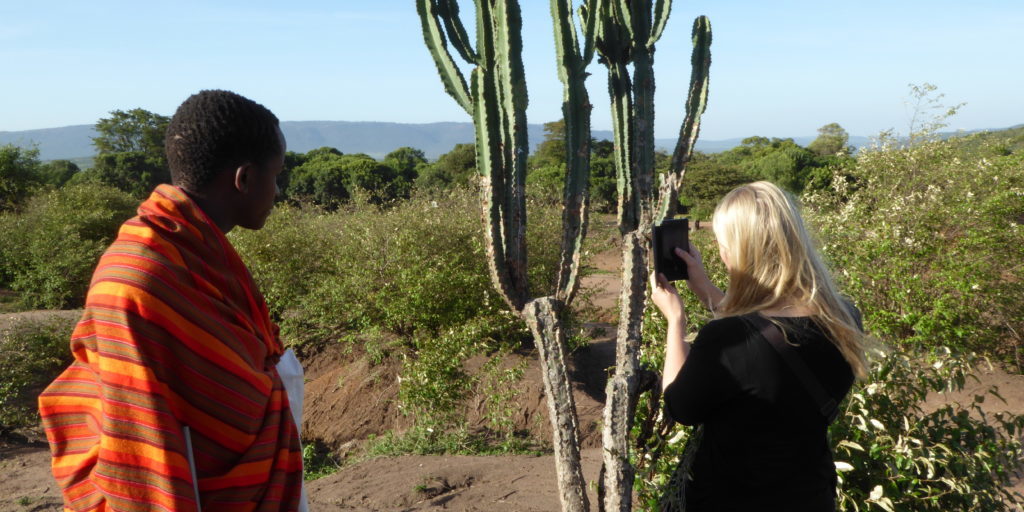 Maasai guide explaining about a big cactus to a european girl. She is taking pictures of the cactus with here phone.