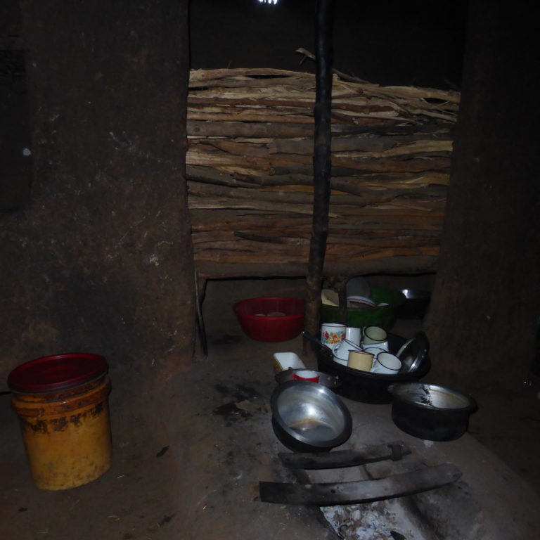 Inside a Maasai house: the kitchen with a fireplace and many cups and pots.